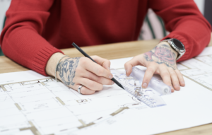 Woman with tattoos on her hands designing plans.