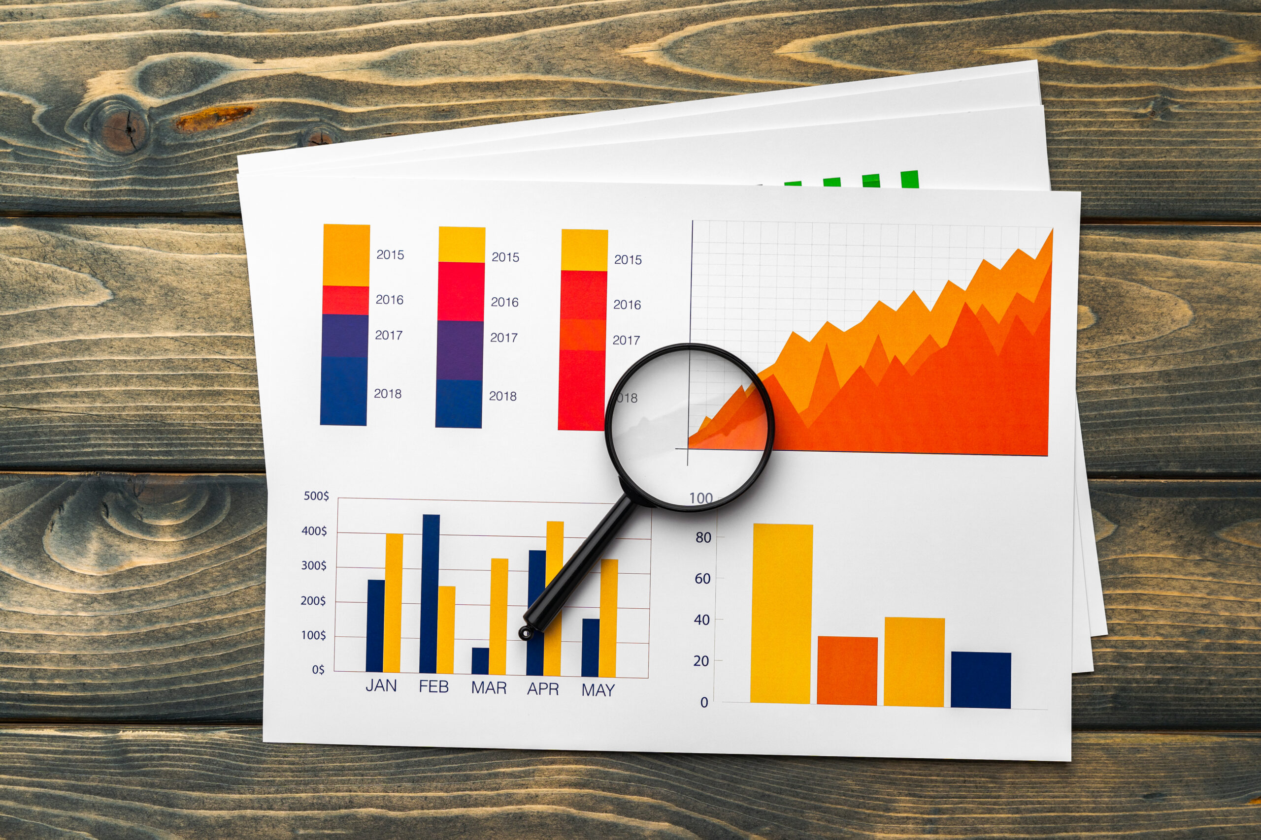 Business graphs and magnifying glass on table, close up