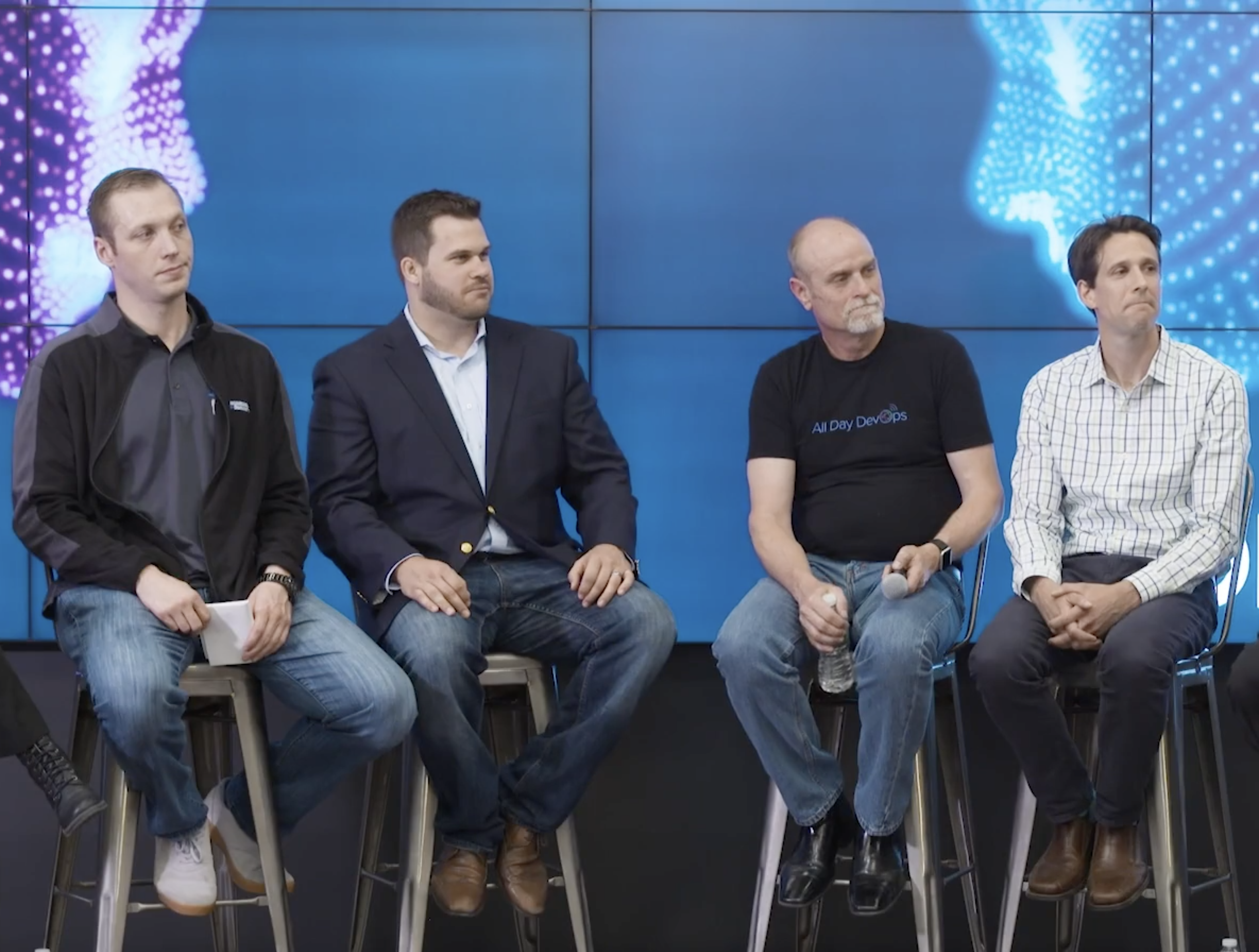 Roundtable discussion at event, with graphics on background screens