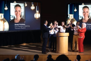 A group of models on stage pretending to be office workers accepting an award for excellence.